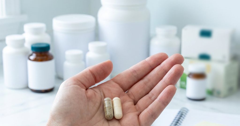 Two capsules in an open palm: one enzyme, one probiotic