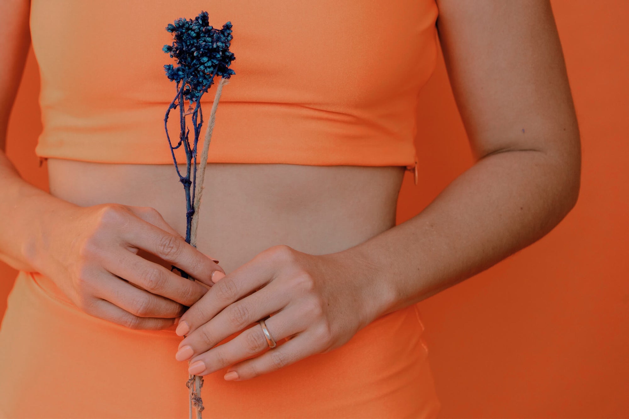 Woman in orange holding a flower near her stomach
