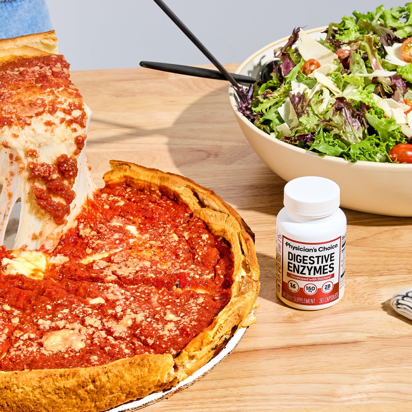 The Digestive Enzymes bottle beside a deep dish pizza and a bowl of salad