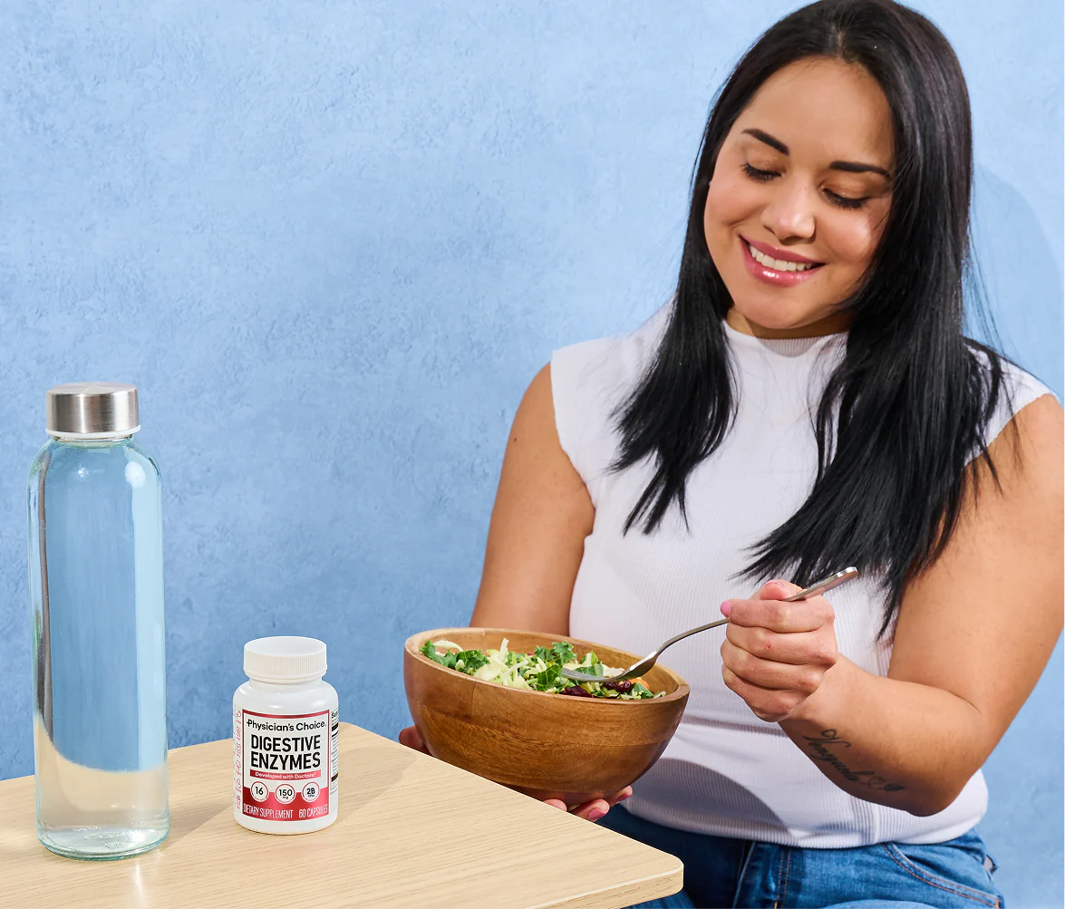A woman eating a salad at a table beside the Digestive Enzymes bottle and a bottle of water