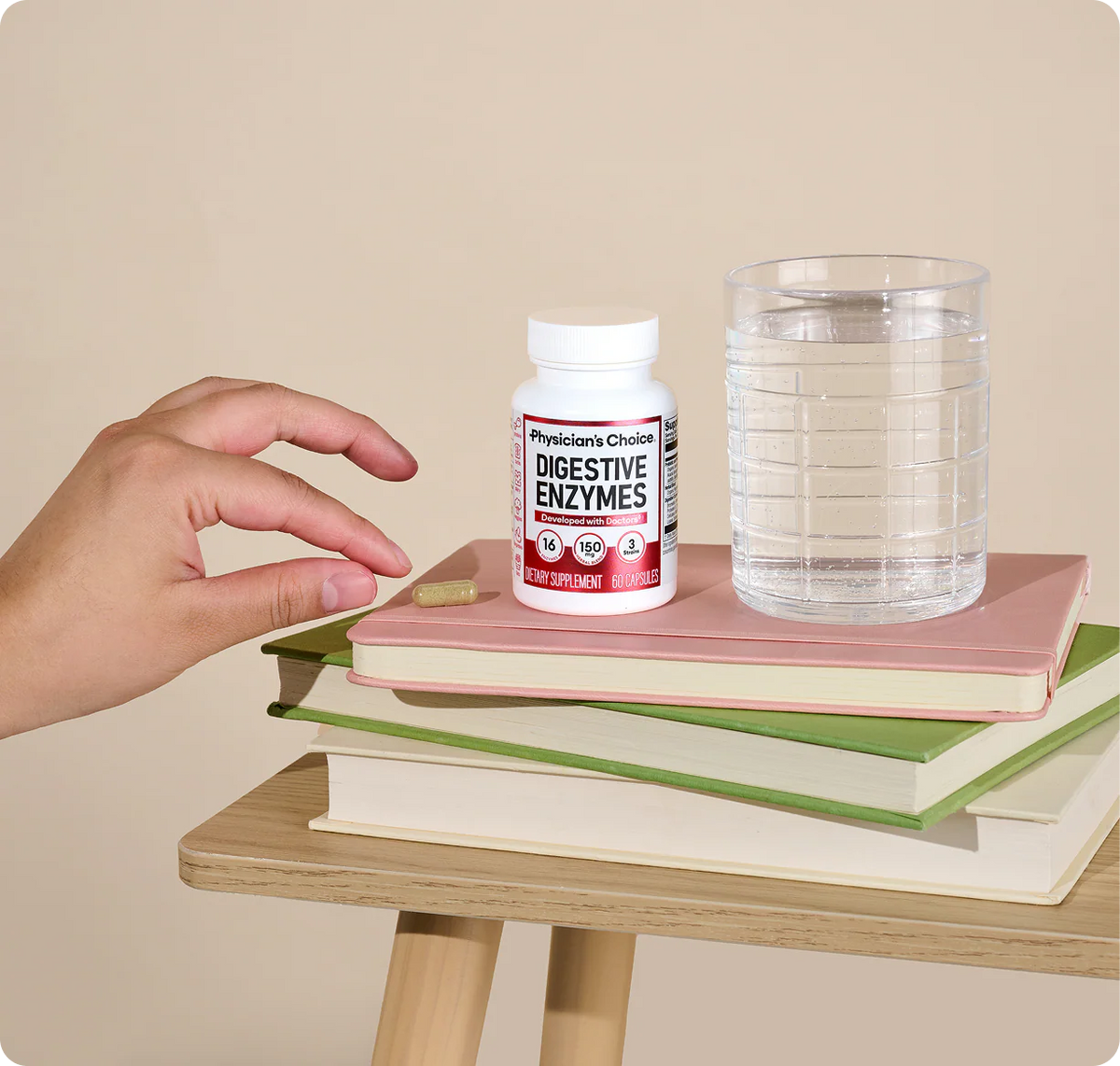 A hand reaching for a Digestive Enzymes bottle and a glass of water on a stack of books
